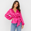 Woman wearing a bright pink satin top with long sleeves and a V-neckline, standing against a plain background.