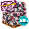 A large stack of bundled clothing on a wooden pallet, with promotional text reading 'WOMEN'S BUDGET BRAND ALL SEASON CLOTHING A GRADE' and '80kg BULK LOT'. The bundles are wrapped in clear plastic and show many different garment colors.