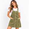 A woman modeling an olive green corduroy bib overalls dress with a front zipper, adjustable shoulder straps, and front patch pockets, worn over a white t-shirt against a plain white background.