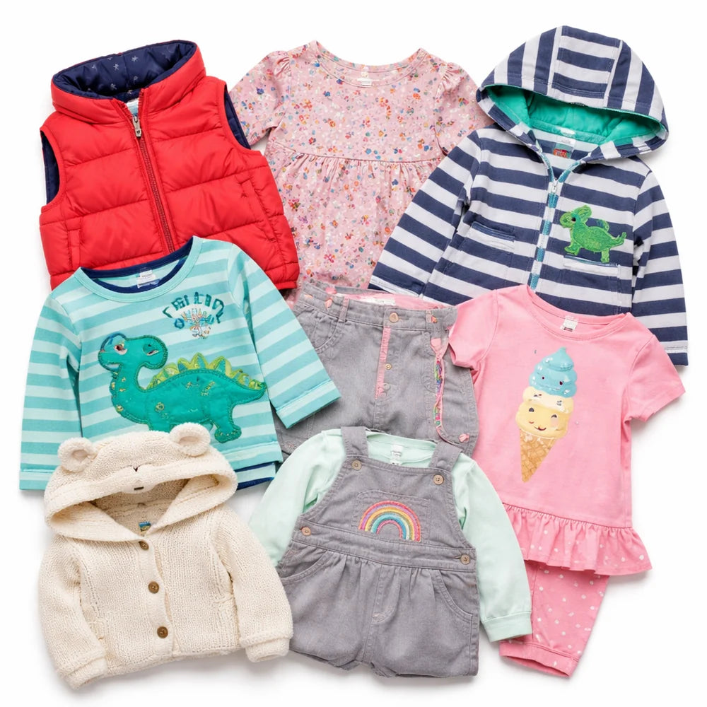 A flat lay of eight baby and toddler clothing items arranged on a white background, including a red puffer vest, a pink floral dress, a navy-and-white striped hooded sweatshirt, a mint striped dinosaur shirt, gray corduroy overalls, a cream hooded knit cardigan, a pink ice cream print romper, and a gray long-sleeve romper with a rainbow patch.