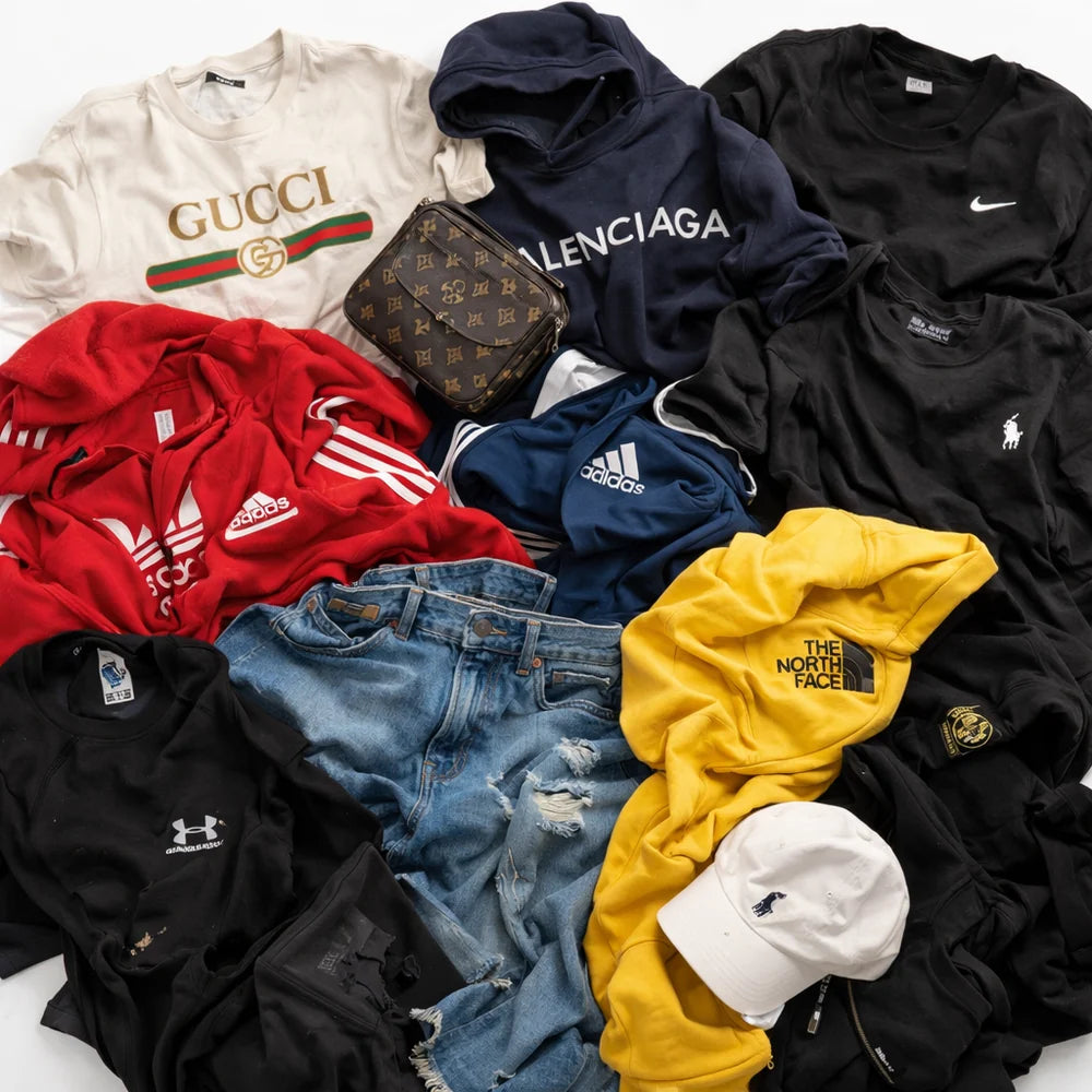 A flat-lay arrangement of multiple streetwear items on a white background, including a cream Gucci sweatshirt, a navy Balenciaga hoodie, a red Adidas sweatshirt, a blue Adidas sweatshirt, a black Polo Ralph Lauren t-shirt, a black Under Armour t-shirt, a yellow The North Face sweatshirt, distressed blue jeans, a Louis Vuitton monogram pouch, and a white baseball cap.