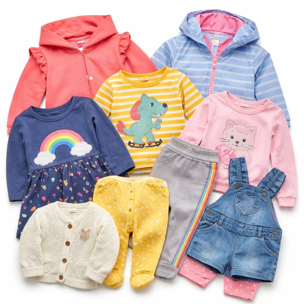A set of baby girl's winter clothing and footed wear arranged together on a white background, including a coral hooded zip-up, a light blue striped hooded jacket, a navy rainbow dress, a yellow dinosaur striped shirt, a pink cat long-sleeve top, gray pants with a rainbow stripe, yellow polka-dot footed pants, a cream bunny cardigan, and blue denim overalls.